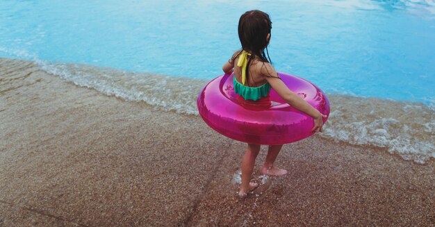 Niña con un flotador de verano junto a la piscina