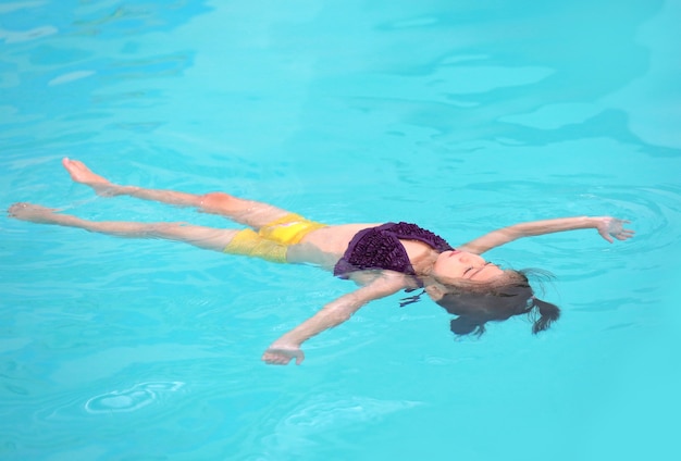 Niña flotando en la superficie del agua de la piscina