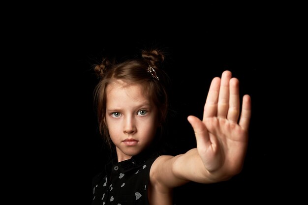 Foto una niña de fondo negro muestra un signo de palma de los pies y una cara seria. detenga la arbitrariedad del resentimiento infantil contra los adultos.