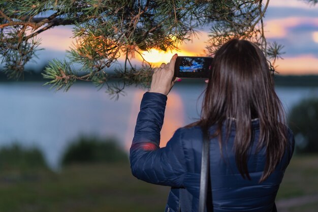 Una niña fotografía la puesta de sol en el lago por teléfono.