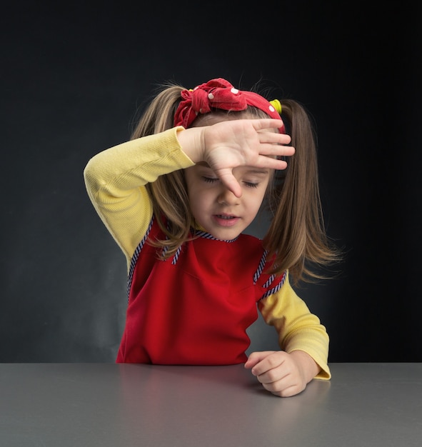 Niña se frota la frente sobre fondo gris