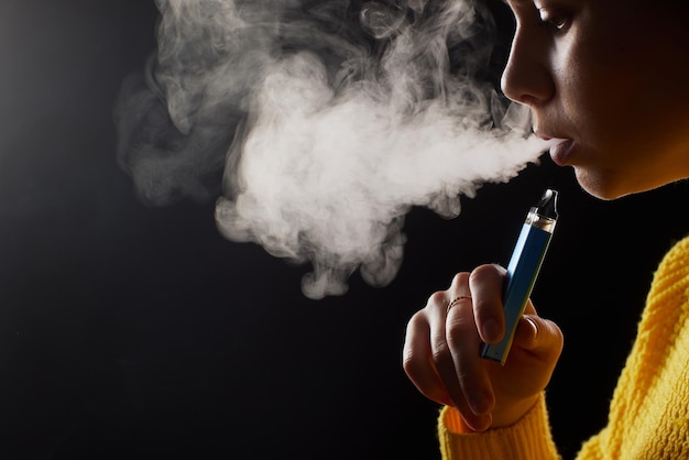 Niña fuma un primer plano de vape sobre un fondo oscuro