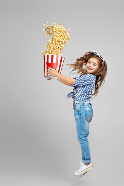 Niña en gafas 3d azul rojo sosteniendo un cubo con palomitas de maíz voladoras