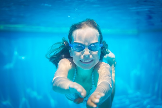 Niña con gafas azules bajo el agua en la piscina