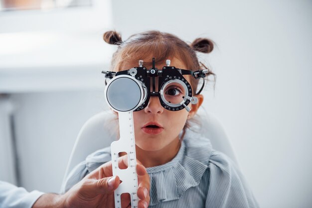 Niña con gafas en la clínica de oftalmología tiene prueba de visión.