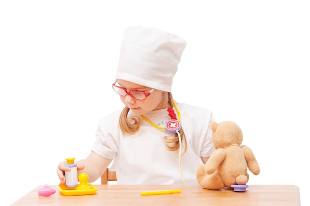 Niña con gafas juega en el médico como mamá y trata juguetes