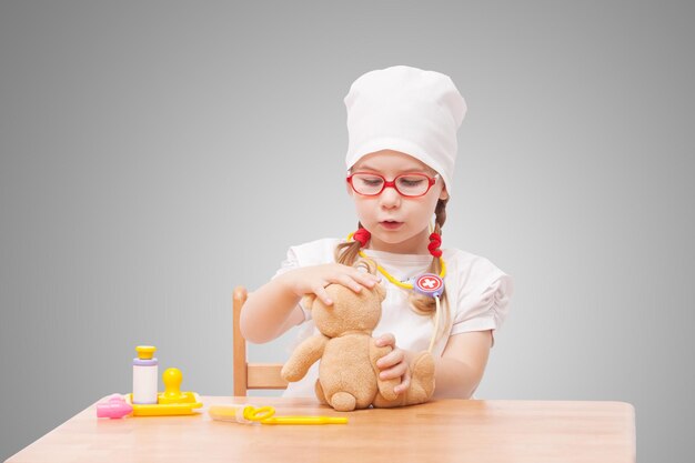 Niña con gafas juega en el médico como mamá y trata juguetes