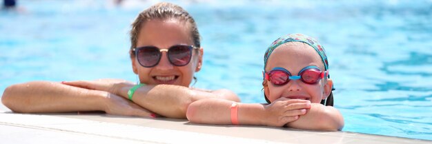 Niña en gafas de natación y madre acostada al lado de la piscina