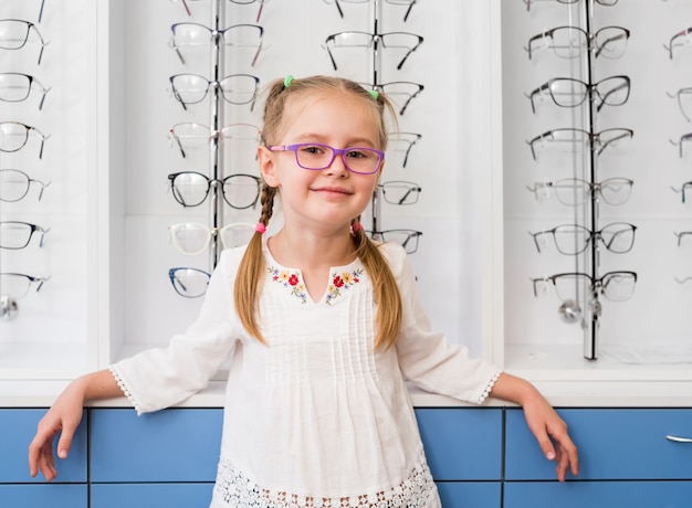 Niña con gafas de pie en la tienda óptica