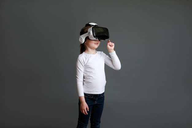 Niña con gafas de realidad virtual jugando videojuegos mirando con gafas VR y gesticulando con la mano, niño experimentando gadget 3D.