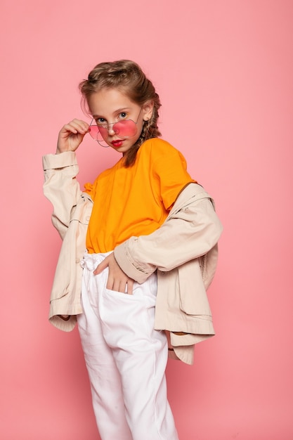 Niña con gafas rosas. Concepto de tiempo de diversión con estilo de moda de moda. Retrato de tamaño completo vertical de risa linda dulce adorable encantadora encantadora niña aislada pared rosa