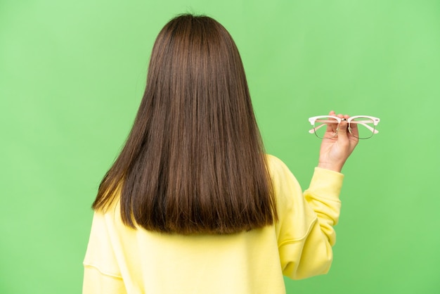 Niña con gafas sobre fondo clave de croma aislado en posición trasera