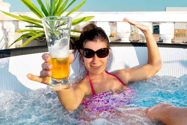 Niña con gafas de sol bebe cerveza en una mini piscina inflable con agua gorgoteante en el Oktoberfest