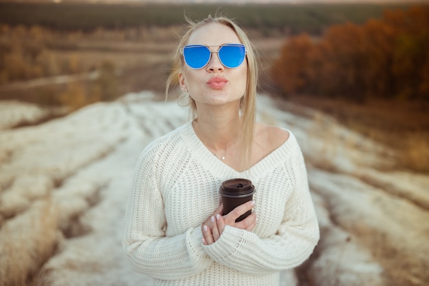 Niña con gafas de sol y café en el parque otoño