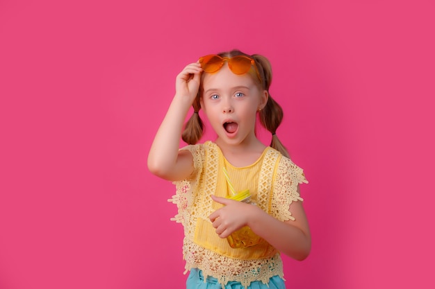 Una niña con gafas de sol con un cóctel en un rosa.