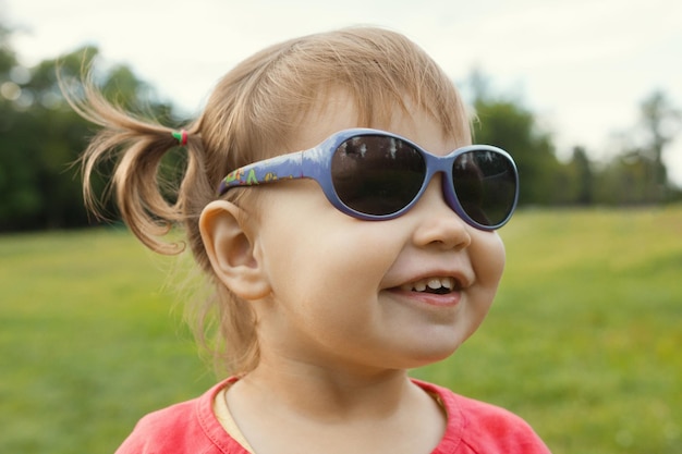 Niña con gafas de sol jugando en el parque frente a la hierba verde, retrato al aire libre