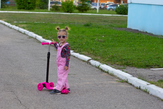 Niña con gafas de sol en scooter en el patio de recreo