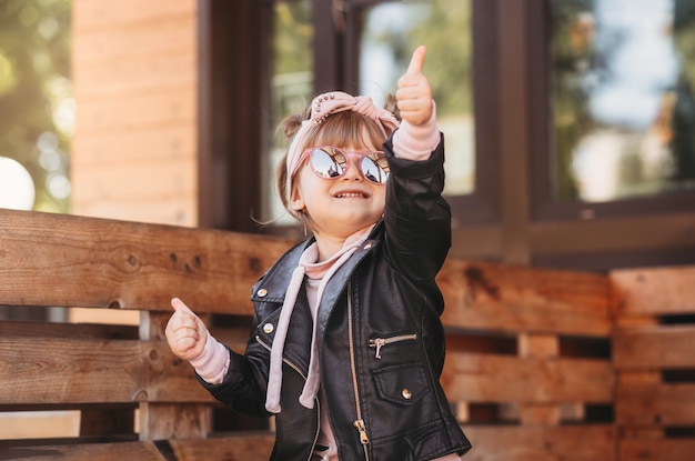 Una niña con gafas de sol se sienta en un café de verano y se divierte