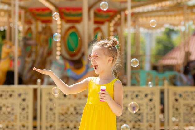 una niña con gafas de sol sopla burbujas de jabón en el parque en el verano