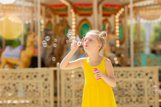 Una niña con gafas de sol sopla pompas de jabón en el parque en verano