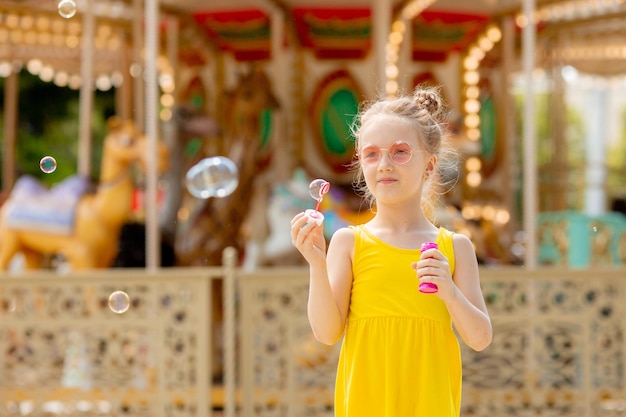 Una niña con gafas de sol sopla pompas de jabón en el parque en verano