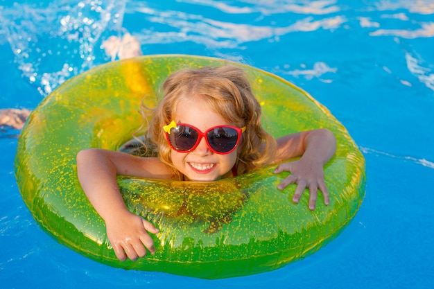 Una niña con gafas de sol y un traje de baño nada en la piscina en un círculo inflable en el verano.