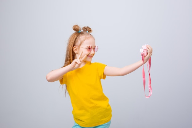 una niña con gafas de sol viajero sostiene una cámara en un fondo blanco