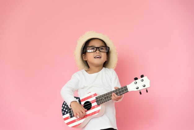 Foto niña con gafas y sombrero mientras toca la guitarra contra un fondo rosa