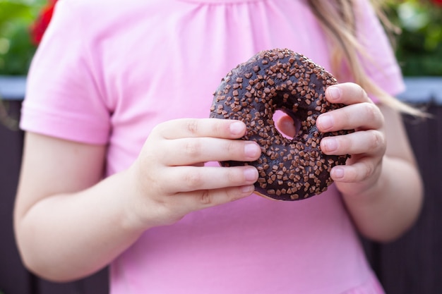 Foto una niña con gafas y un vestido rosa está comiendo una rosquilla dulce.