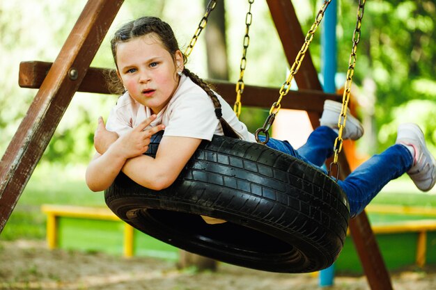 Niña genial columpiándose en una rueda de goma en el patio de recreo en el primer plano del parque verde Vacaciones de verano en el centro turístico del campamento Caminar y jugar al aire libre actividad deportiva y recreación de estilo de vida saludable