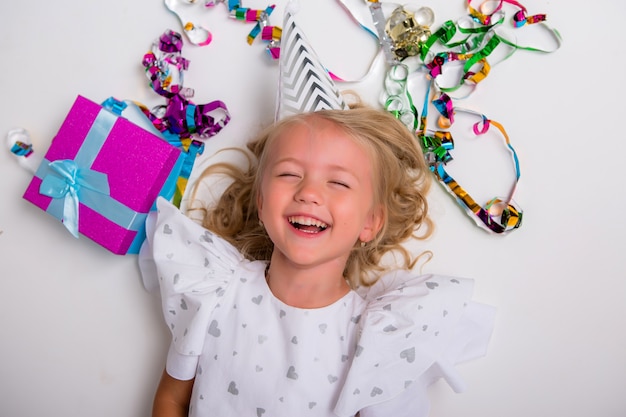 Niña con gorra de cumpleaños sonriendo con caja de regalo y confeti