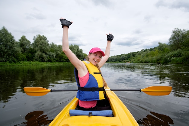 Niña con gorra rosa remando en kayak sobre el río, divirtiéndose durante el viaje