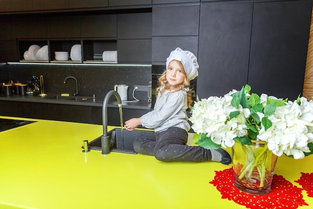 Niña con gorro de cocinero aprendiendo a cocinar sonriendo en la cocina