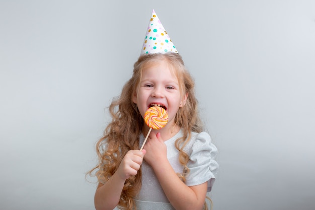 Niña con un gorro de cumpleaños con una piruleta