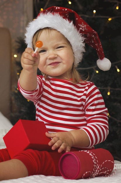 Niña con gorro de Papá Noel abriendo caja de regalo de Navidad Niño divertido y expresivo disfrutando de regalos