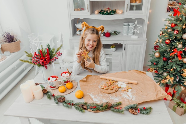 Niña con gorro de Papá Noel para hornear galletas de Navidad en la cocina de casa.