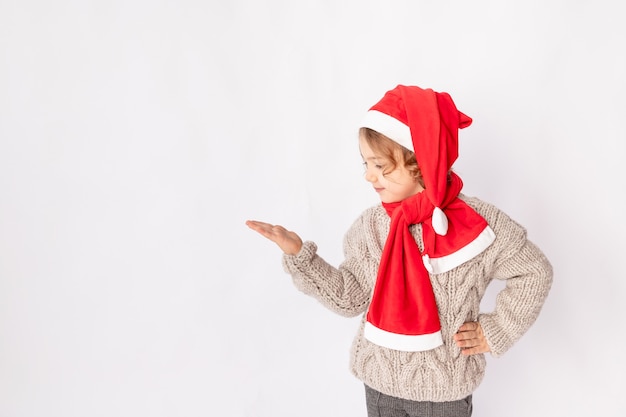 Una niña con un gorro de Papá Noel sobre un fondo blanco sostiene su mano para espacio para texto