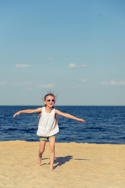 Niña graciosa en gafas de sol está corriendo y sonriendo.