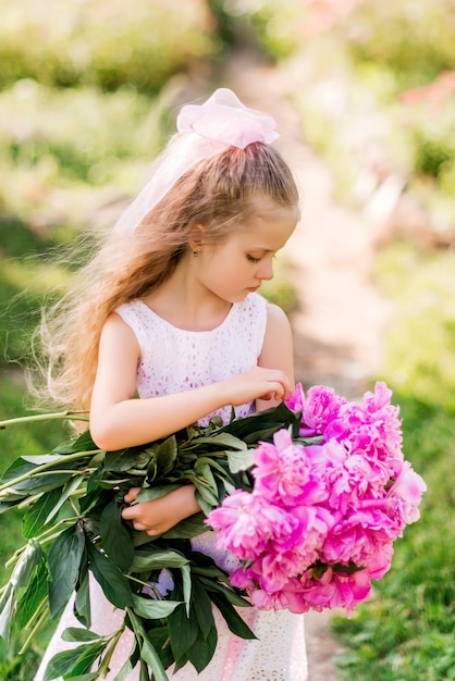 Foto niña con un gran ramo de peonías. un niño camina en el parque con flores en verano.