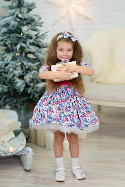 Niña con un gran regalo de Navidad posa cerca del árbol de Navidad