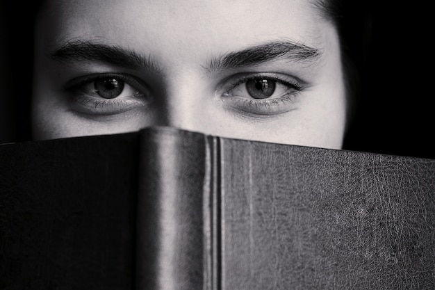 Una niña con grandes ojos se esconde detrás de un libro.