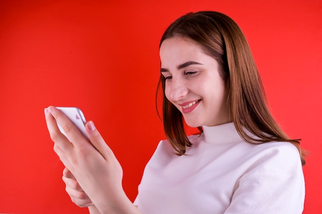 Niña hablando por un teléfono inteligente sobre un fondo rojo. Copia espacio