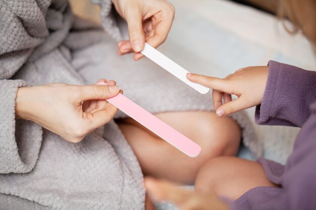 La niña hace la manicura a la madre, en casa en la cama.