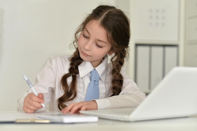 Niña haciendo los deberes, escribiendo y usando la computadora portátil