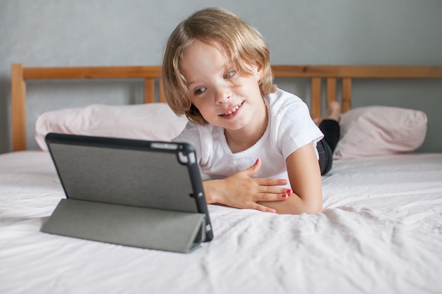 Foto niña haciendo los deberes en línea acostado en la cama en casa comunicación con familiares en línea