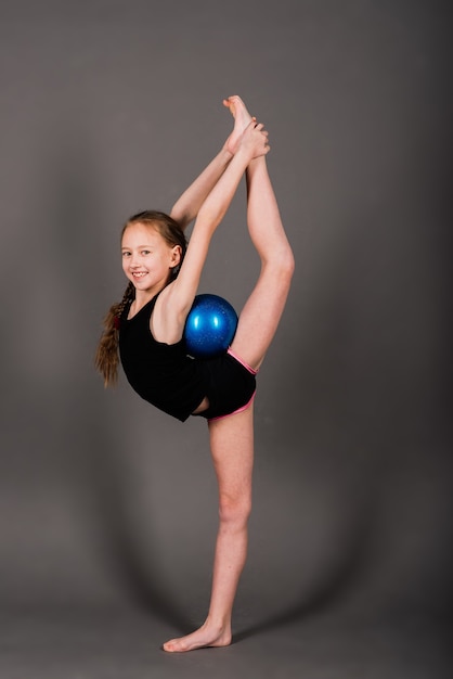 Niña haciendo gimnasia con aro, pelota y split aislado sobre fondo gris,  estudio