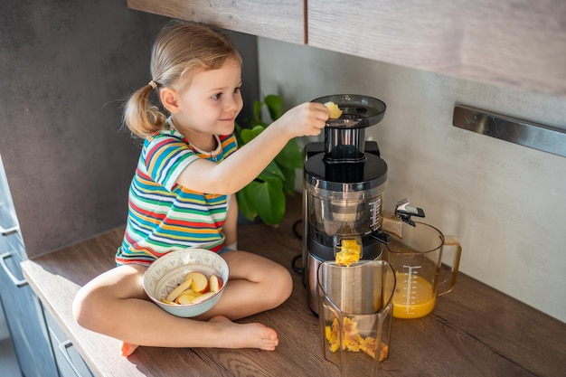 Niña haciendo jugo fresco sentado en la mesa en la cocina de casa