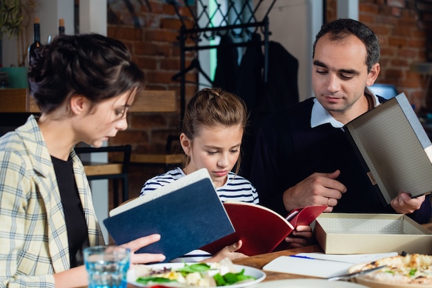 Una niña haciendo su tarea en la mesa de la cocina con sus padres cerca