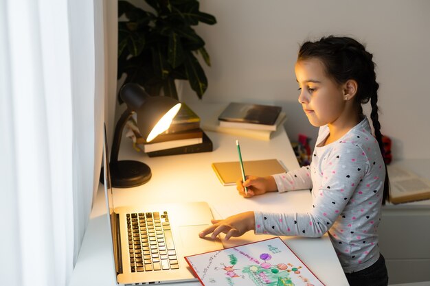 Niña haciendo sus deberes en casa y usando una computadora portátil