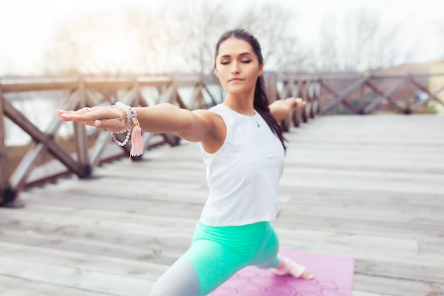 Niña haciendo yoga Guerrero ejercicio Virabhadrasana plantean al aire libre en la naturaleza en el puente de madera